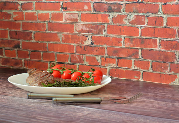 Grilled beef steak with rosemary and cherry tomatoes on a wooden table, next to a fork and knife. Close-up.
