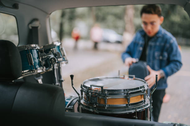 Asian chinese musician unloading drum kits from car trunk on trolley getting ready for performance