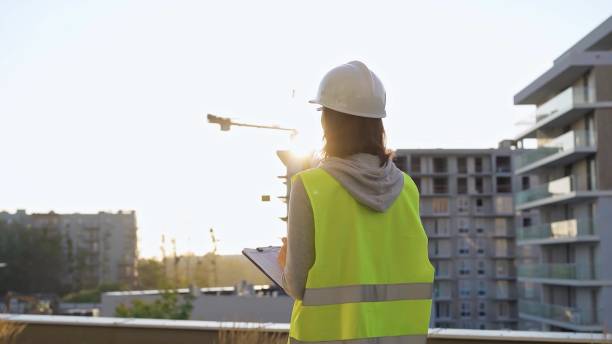 istock Female construction engineer with a hard hat and safety vest is writing on a clipboard while inspecting a construction site in the evening at sunset 2177906796