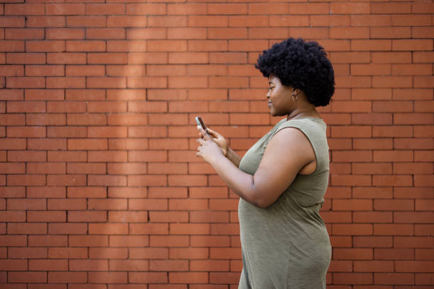 istock Young black woman using cell phone against brick wall. 2177908121