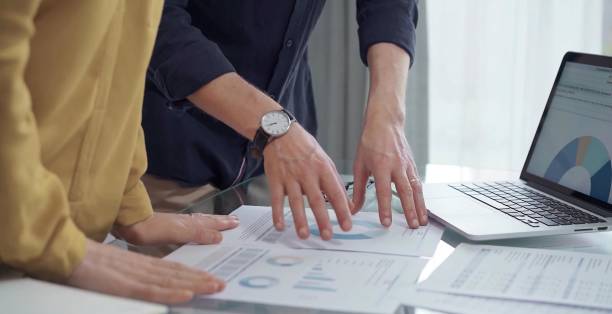 istock Business people, professionals analyzing financial charts and data on a desk while standing and using laptop computer in office. Dark blue shirt and yellow blouse 2177910134