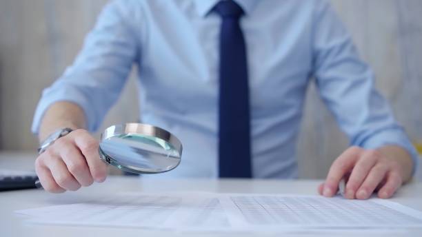 istock Businessman is carefully examining financial documents with a magnifying glass, highlighting the importance of thorough analysis in business. Audit and taxes 2177915685