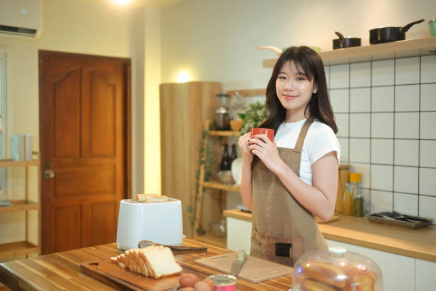 istock Charming young woman wearing apron enjoying a warm drink while preparing breakfast in kitchen 2177922157