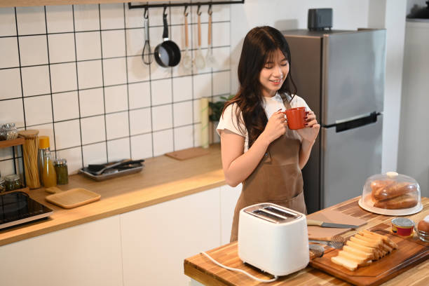istock Charming young woman wearing apron enjoying a warm drink while preparing breakfast in kitchen 2177922268