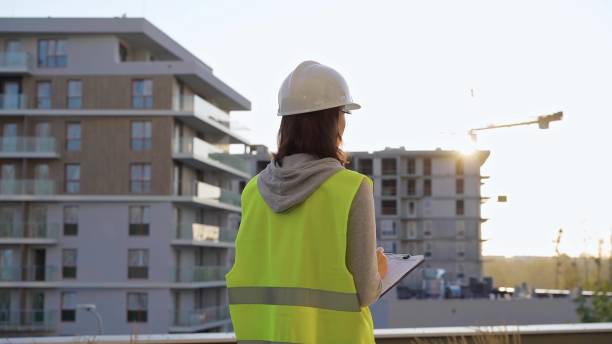 istock Female construction engineer with a hard hat and safety vest is writing on a clipboard while inspecting a construction site in the evening at sunset 2177922891