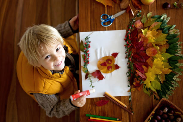 istock Sweet child, boy, applying leaves using glue while doing arts and chraft with leaves 2177927361