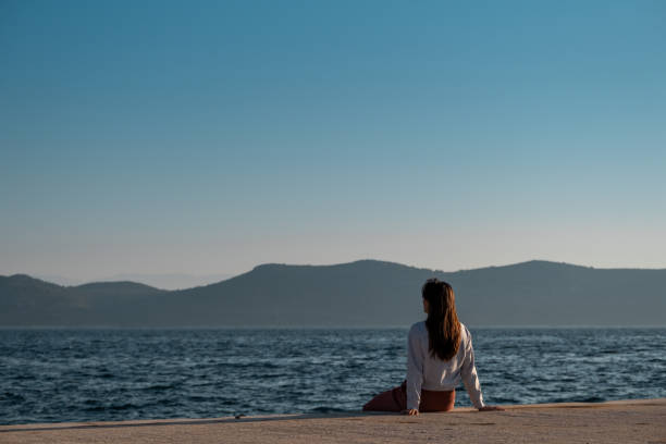 Woman looking at the calm sea from a pier with distant mountains in the background