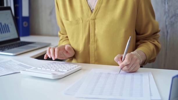 istock Businesswoman with yellow blues is using white calculator and taking notes in her office. Taxes and audit concept 2177931701