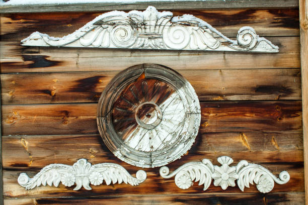The image displays decorative wooden elements on the exterior of a rustic house. It features an intricate wooden ornament with a circular centerpiece surrounded by ornamental carvings