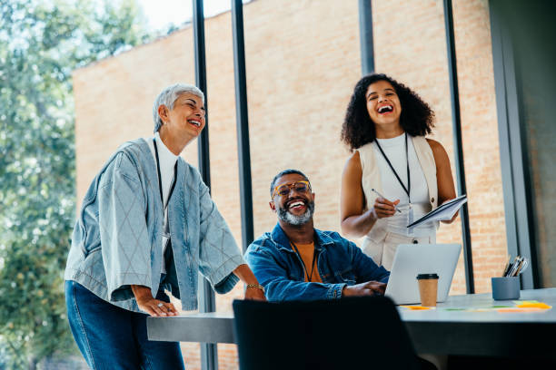 istock Diverse group of colleagues laughing and collaborating in an office setting with natural light and modern decor, working together on a creative project with a laptop and notes 2177945425