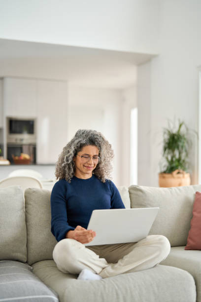Happy relaxed mature woman using laptop computer sitting on couch at home.