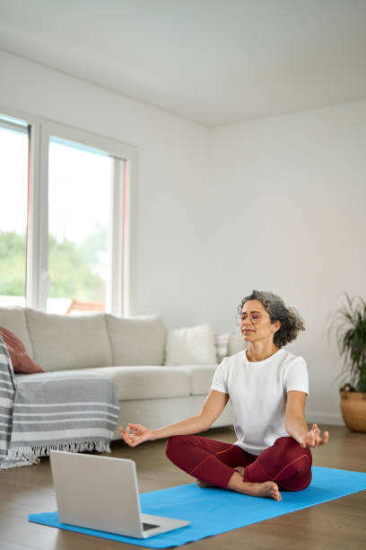 istock Serene mindful mature old woman meditating with tutorial online in living room. 2177949739