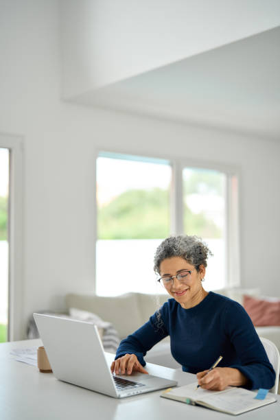 istock Happy middle aged woman sitting at table and using laptop writing notes. 2177949757