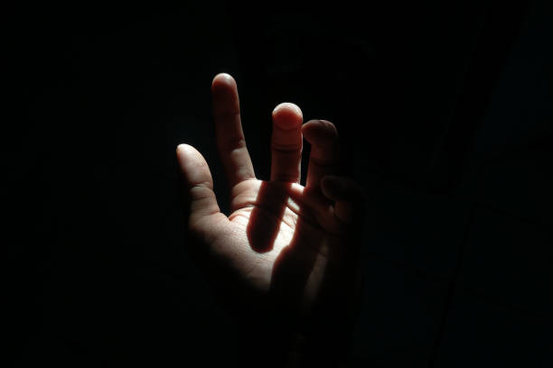istock Male hand reaching for light in darkness on isolated black background. 2177954854