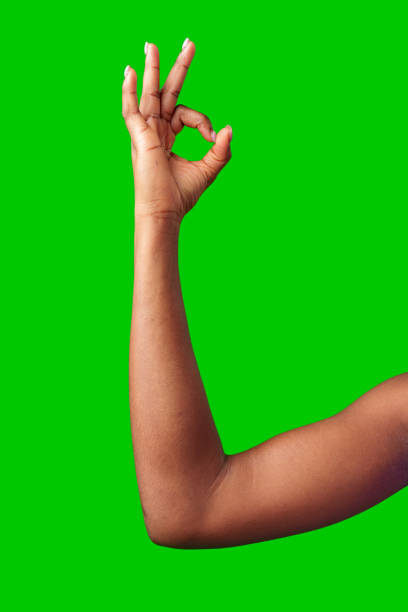 A hand making a gesture with a green background during daylight close up