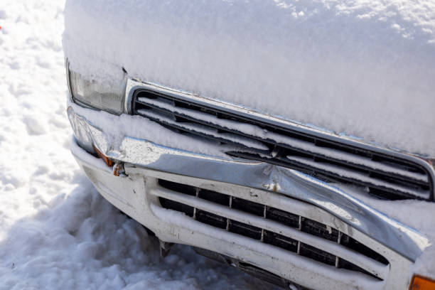 snow covered white SUV car with damaged front bumper at sunny winter day