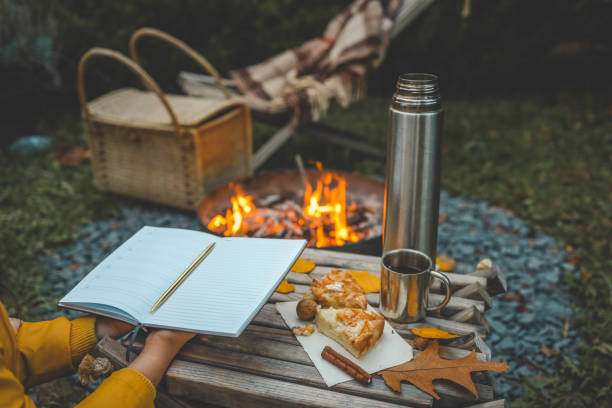 istock Person writing in a notebook next to a bonfire during autumn. Outdoor cozy setting with fallen leaves, snacks, hot drink, and the warmth of the fire, capturing the essence of a peaceful autumn day 2177968500