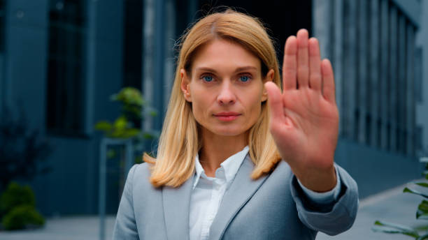 istock Serious woman standing outdoors looking at camera showing stop gesture holding palm in front confident businesswoman protecting personal boundaries demonstrates prohibition sign keep your distance 2177968718