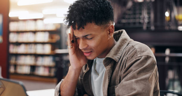 istock Man, student and tech in library with headache, stress and massage temple for relief. Person, laptop and migraine at university campus with fatigue, tension and tired with research or assignment 2177975166