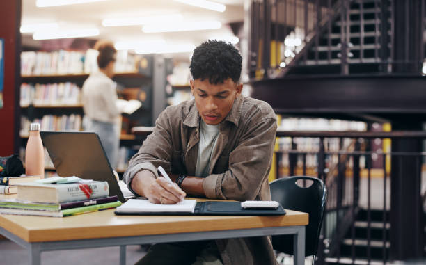 istock African, man and student writing in library for research information, university thesis and study schedule. Male person, laptop and reading for education knowledge, history exam and project planning 2177975170