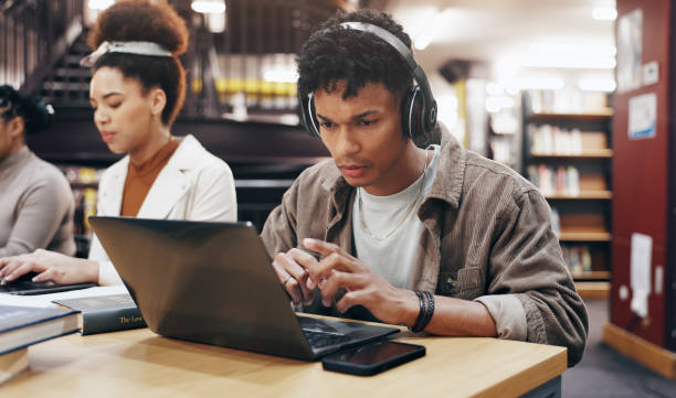 istock Man, studying or laptop in library with headphones, problem solving or working on research assignment. Student group, concentration music or tech at college for education, online course or learning 2177975189