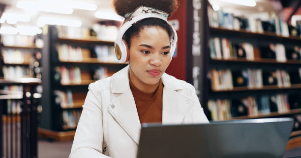 istock African, student and typing on laptop in library for research information, university web and study schedule. Girl, online course and headphones for education project, exam results and podcast audio 2177975219