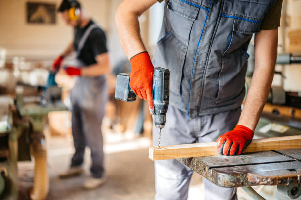 Handsome young male carpenter using an electric drill on the wood in his workshop.