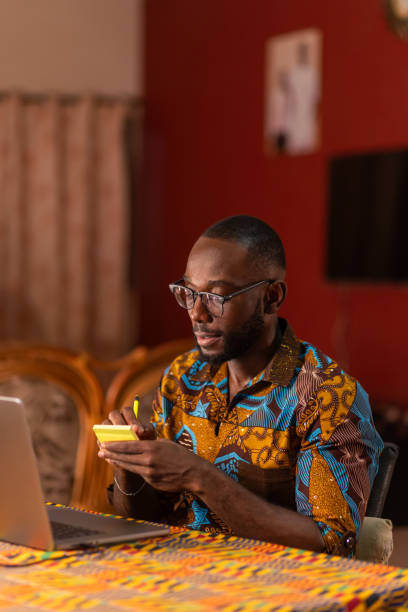 istock A young African man sits at a table in his home, focused on his work, with a laptop and a notepad in front of him. 2177986841