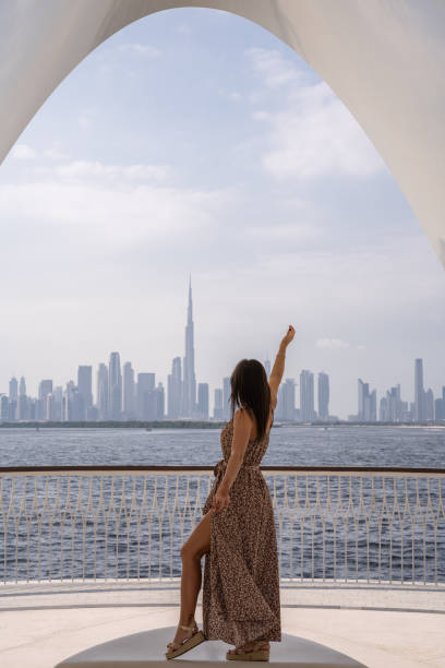 istock Unrecognizable young woman looking at the Dubai skyline from a distant viewpoint with a long dress and one arm raised, enjoying her trip. 2177990269