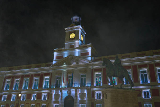 Night view of a historic building with a clock tower and an equestrian statue in front, illuminated by soft lighting.
