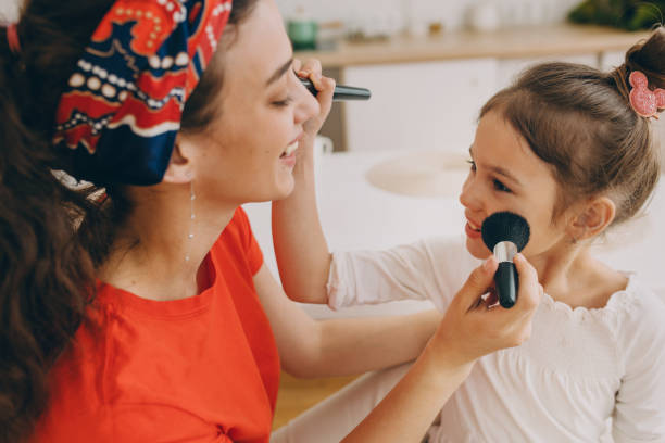 istock Close-up image of two sisters of different age having fun using make-up brush to prepare for going to party of their friends, woman wearing red bandana, smiling at girl with hair bun 2177997617