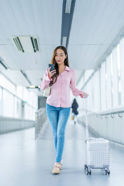 istock Asian Woman with Luggage Using Phone Walking Through Covered Pedestrian Walkway 2178010721
