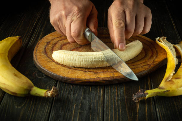 istock Cutting raw banana with knife in chef hand to prepare fruit dish on kitchen table. Advertising space. Bananas diet preparation concept 2178013668