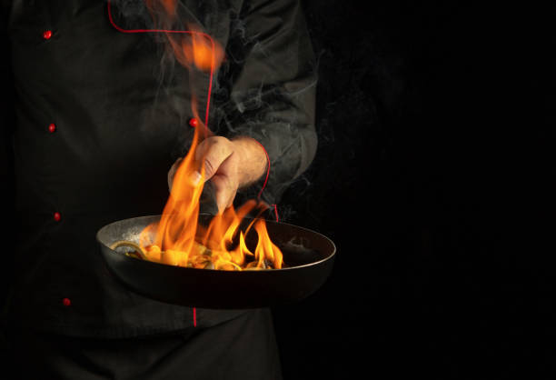 istock Chef cooking vegetables on a burning frying pan with flame. Restaurant and hotel service concept on a black background. Flambe or cooking with natural fire 2178014184