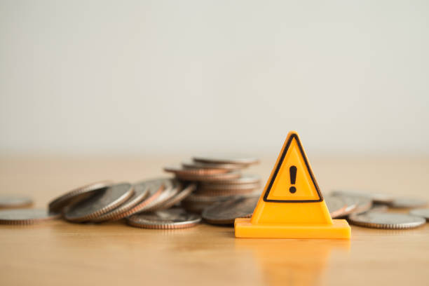 istock Yellow warning sign label on stack coins crash on wooden table with white background copy space. 2178026309