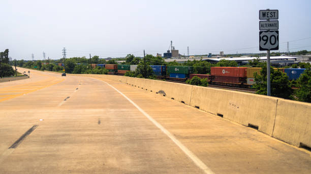 istock Freight train parallels alternate highway route in Texas. Colorful cargo containers travel alongside industrial West Highway 90. 2178030636