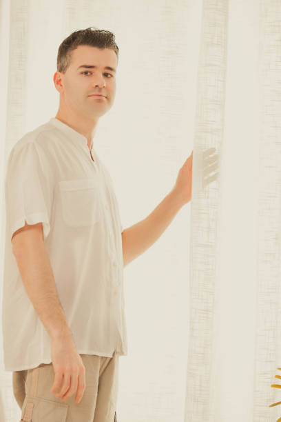 istock Man looking through the window standing in living room 2178035885