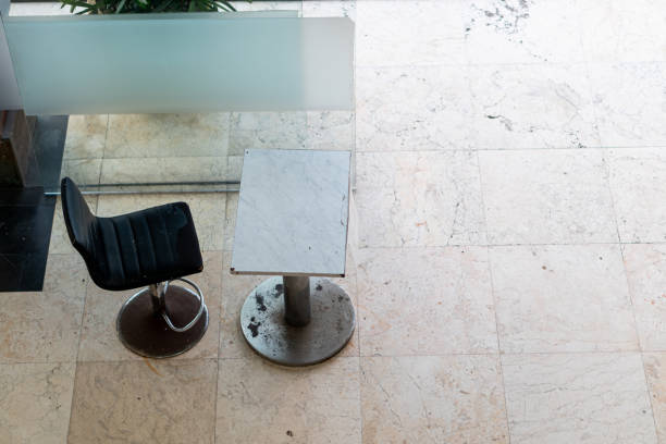 Five identical gray chairs stand in a symmetrical row against a textured concrete wall on a tiled floor. Clean lines and minimalist design create a sense of order and simplicity.