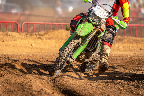 Detail of the front of an off-road motocross bike going through a curve in muddy terrain with the wheels and rider's boots dirty with mud, on a wet dirt track during a motocross endurance race. detalle de la parte delantera de una moto de motocross todoterreno atravesando una curva en un terreno fangoso con las ruedas y las botas de piloto sucias de barro, en una pista de tierra mojada durante una carrera de resistencia de motocross.