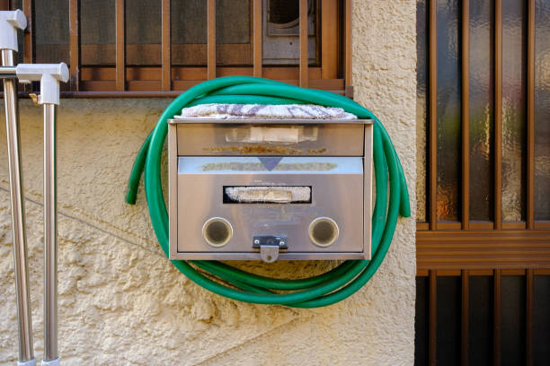 Silver colored metal mailbox on a wall with a green hose wrapped around it.