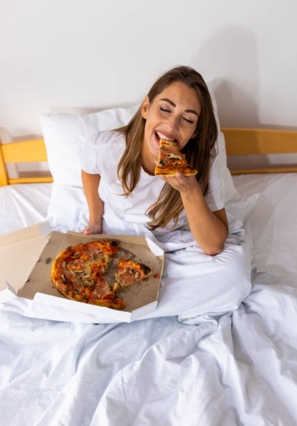 istock Woman eating pizza slice from box in bed 2178070253