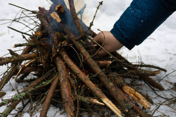 istock In the forest, a man makes a fire by setting dry firewood on fire to keep warm. A man is engaged in survival in extreme conditions in the forest in winter. Making a fire to keep warm in winter. 2178074254