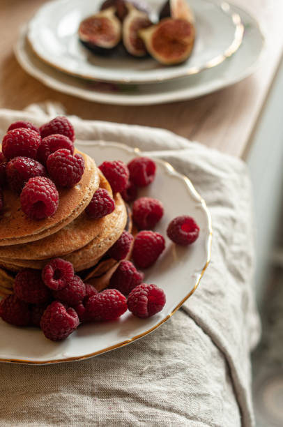 Delicious whole wheat healthy pancakes with raspberry, fork and knife styling natural light and copy space on the table with linen cloth background lifestyle