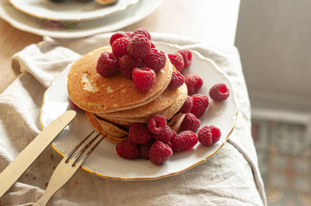 Delicious whole wheat healthy pancakes with raspberry, fork and knife styling natural light and copy space on the table with linen cloth background lifestyle