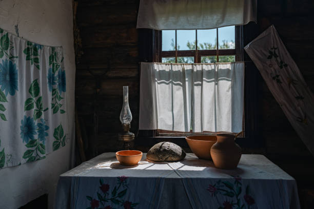 Rustic interior with a window bathed in sunlight. The room is dimly lit, but the window lets in a bright beam of light, highlighting a table set with a clay jug, a bowl.
