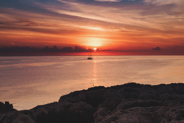 Beautiful colorful sunrise at the sea with dramatic clouds, the sailing boat and sun shining