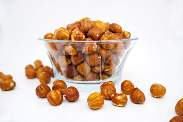 Side view of hazelnuts in a glass bowl on white background