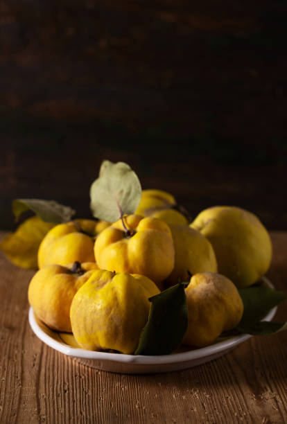 Ripe yellow quince fruits on a plate on a wooden table. Photo in a low key in a rustic style