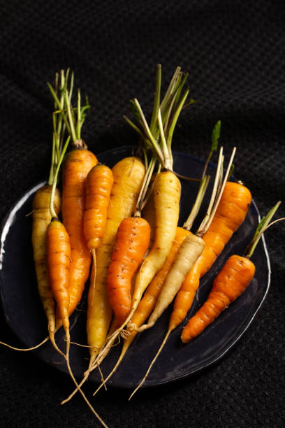 istock White, yellow and orange carrots in a black plate on a black napkin. 2178102731