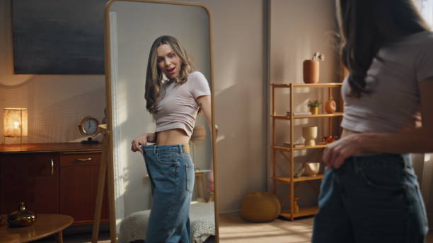 istock Female reflection checking weight loss progress. Smiling woman trying big jeans 2178105877